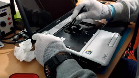 Manos-Masculinas-Enguantadas-De-Ingeniero-Reparando-Laptop-En-Escritorio-De-Madera