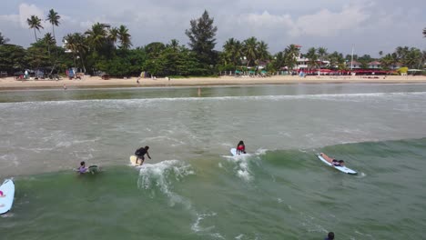 Kamerafahrt-Von-Menschen,-Die-Auf-Einer-Glatten-Welle-Surfen-Und-Am-Erstaunlichen-Sandstrand-In-Sri-Lanka-Ins-Wasser-Fallen