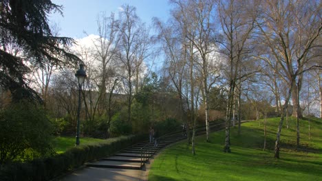 View-of-beautiful-relaxing-green-garden-and-a-cemented-pathway-with-stairs-leading-upto-the-road-of-the-Parc-Montsouris,-a-public-garden-located-in-the-Porte-d'Orleans-neighborhood-in-Paris,-France