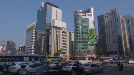 Seouler-Tagesverkehr-An-Der-Kreuzung-Des-Bahnhofs-Gangnam-Mit-Autos,-Die-An-Einem-Sonnigen-Tag-Auf-Einer-Mehrspurigen-Autobahn-Gegen-Hochhäuser-Fahren