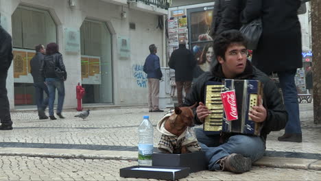 Tiene-15-Años,-Es-Mendigo-Y-Con-El-Acordeón-En-Brazos-Toca-Para-Los-Turistas-Que-Caminan,-A-Su-Lado-El-Pequeño-Perro-Que-Lo-Acompaña-Todos-Los-Días.