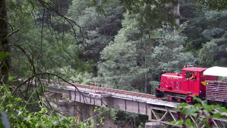 Red-locomotion-pulling-a-cart-full-of-waving-tourists-across-a-bridge