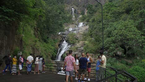 Toma-En-Cámara-Lenta-De-Un-Joven-Sosteniendo-Su-Dron-Caminando-Hacia-Sus-Amigos-Frente-A-Las-Cataratas-De-Ravana,-Sri-Lanka