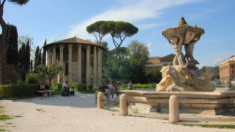 Panning-across-ancient-roman-water-spring-Fountain-of-the-Tritons-and-historic-sights-at-Piazza-Bocca-della-Verità-in-Rome,-Italy