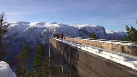 Los-Turistas-Disfrutan-De-Una-Vista-Impresionante-En-El-Borde-Del-Mirador-Stegastein-Noruega---Clip-En-Movimiento-Lateral-Detrás-Del-Mirador-Con-Nieve-Pasando-En-Primer-Plano-Del-Marco-Inferior