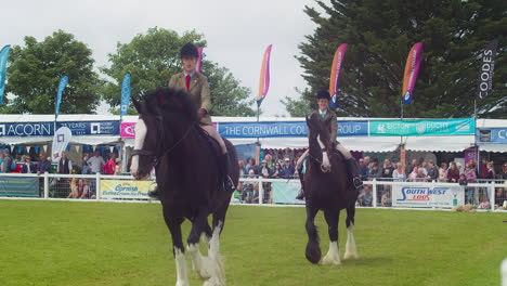 El-Show-De-Royal-Cornwall-2022-Con-Jinetes-Femeninos-En-Grandes-Caballos-De-Condado-Pasando-Con-Una-Audiencia-En-El-Fondo---Cámara-Lenta