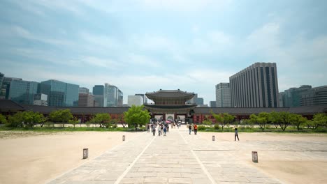 Puerta-Heungnyemun-Con-Gente-Caminando-Lejos-Y-Edificios-Del-Centro-De-Negocios-De-Seúl-Y-Edificio-Del-Gobierno-Detrás,-Palacio-Gyeongbokgung