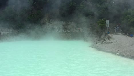 tourists-on-the-shoreline-of-a-neon-green-sulfur-lake-at-Kawah-Putih,-aerial