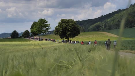 Toma-Amplia-Que-Muestra-Una-Multitud-De-Ciclistas-En-La-Carretera-Entre-Campos-Rurales-Y-Colinas-En-Suiza---Evento-De-Desaceleración-Amigable-Con-El-Clima