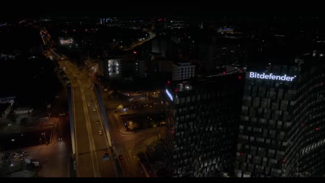 Flying-Over-Illuminated-Orhideea-Towers-In-The-Cityscape-Of-Bucharest-During-Night-In-Romania