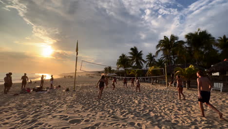 Partido-De-Voleibol-De-Playa-En-La-Hermosa-Costa-De-Arena-Al-Atardecer-En-Verano,-Puerto-Escondido-México,-Grupo-De-Turistas-Jugando-Con-Pelota-En-La-Playa-Rodeado-De-Palmeras,-Entretenimiento-Turístico-Y-Ocio