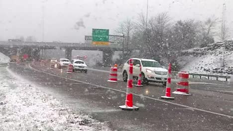 Cars-driving-in-the-snow-past-orange-safety-cones-in-Sellersburg,-Indiana,-SLOWMO