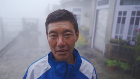 Der-Alleinstehende-Alte-Asiatische-Mann-Blickt-In-Die-Kamera-Und-Lächelt-An-Einem-Nebligen-Und-Nebligen-Morgen-An-Der-Bergstation