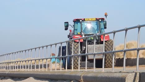 Roter-Traktor-Fährt-Entlang-Des-Strandwegs-Mit-Metallgeländern-Entlang-Der-Strecke