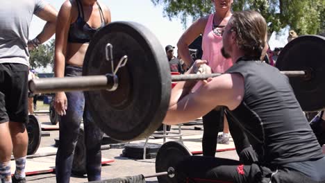 A-fit-young-male-squatting-using-an-olympic-barbell-during-a-cross-fit-competition,-strength-training-for-muscular-endurance,-healthy-and-good-for-weight-loss-and-muscular-and-core-development