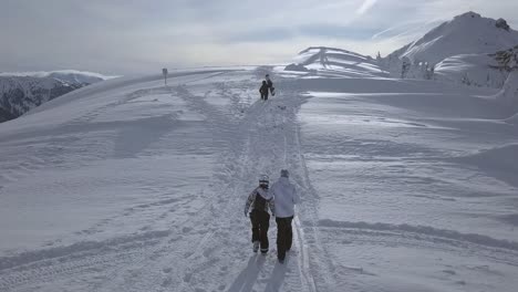 Toma-Aérea-De-Una-Pareja-Caminando-Por-Una-Montaña-Cubierta-De-Nieve-Y-El-Tipo-Le-Pone-La-Mano-En-El-Hombro-Mientras-Caminan