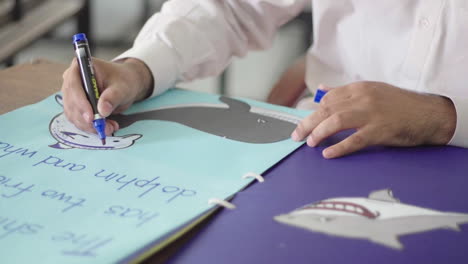 A-man-drawing-a-dolphin-with-a-marker-on-a-chart-on-the-table,-Close-up-view