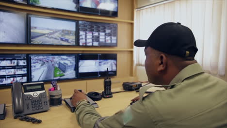 A-port-control-room-view,-a-uniformed-officer-monitoring-the-security-cameras-on-the-screens-and-operating-them-by-a-remote