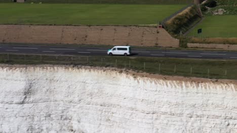 Toma-Aérea-De-Una-Autocaravana-Blanca-En-La-Carretera-Costera-A259,-Sobre-Acantilados-De-Tiza-Cerca-De-Brighton,-Reino-Unido