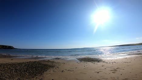 Two-young-women-walking-on-a-sandy-beach-with-sun-above-and-blue-sea