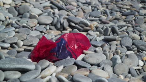 Bolsa-De-Plástico-Roja-Que-Ensucia-Una-Playa-De-Guijarros