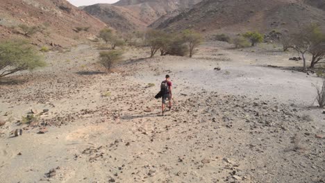 Toma-Aérea-De-Un-Dron-De-Un-Joven-Caminando-En-Un-Valle-Rocoso-Del-Desierto-En-Hatta,-Emiratos-árabes-Unidos