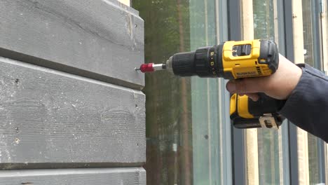 El-Trabajador-Aprieta-El-Tornillo-Con-Un-Destornillador-En-Una-Tabla-De-Madera,-Trabajando-En-La-Fachada-Exterior-De-Una-Casa-Nueva,-Un-Primer-Plano-Estático-En-Cámara-Lenta