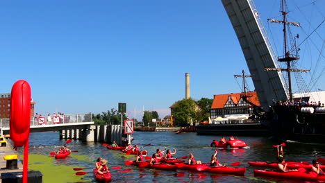 Die-Menge-Der-Touristen-In-Den-Roten-Kajaks,-Die-Unter-Der-Zugbrücke-Paddeln,-Und-Das-Piratenboot,-Das-In-Die-Entgegengesetzte-Richtung-Fährt