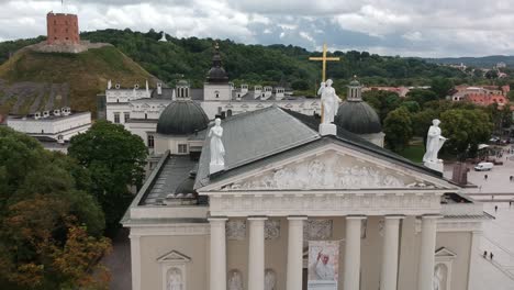 Aerial-shot-moving-backwards-over-the-roof-of-the-cathedral,-revealing-the-tower,-the-Gediminas-tower-at-background,-and-part-of-the-street