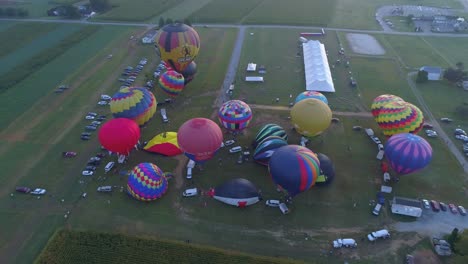 Luftaufnahme-Eines-Morgendlichen-Starts-Von-Heißluftballons-Bei-Einem-Ballonfestival-Vom-Befüllen-Bis-Zum-Abheben,-Wie-Von-Einer-Drohne-Gesehen