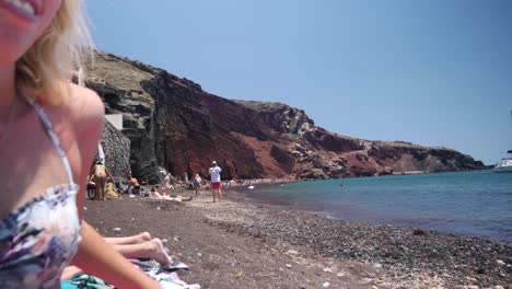 Die-Weitwinkelaufnahme-Von-Red-Beach-Verwandelt-Sich-In-Eine-Nahaufnahme-Einer-Frau,-Die-Auf-Ihr-Telefon-Schaut,-Statt-In-Die-Wunderschöne-Umgebung-Von-Red-Beach-In-Akrotiri,-Santorini,-Griechenland