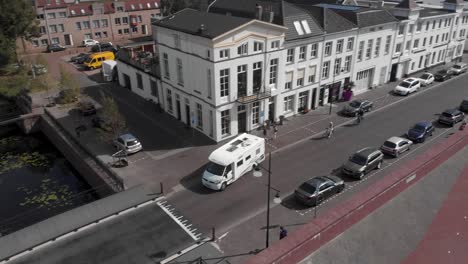 Aerial-following-of-a-camper-driving-away-from-being-parked-at-the-boulevard-of-the-Dutch-Hanseatic-medieval-city-of-Zutphen-with-the-typical-white-front-homes-on-a-sunny-day-against-a-blue-sky