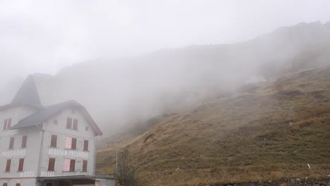 Clouds-climb-up-the-slope-of-a-hillside-in-rocky-mountain-landscape-behind-hotel---KLAUSENPASS,-SWITZERLAND