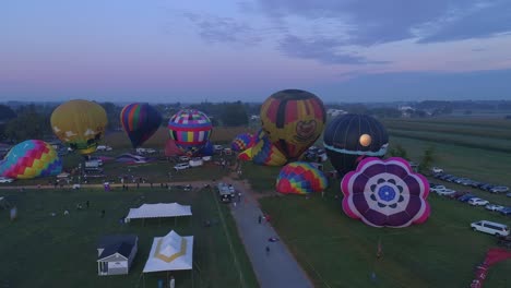 Luftaufnahme-Eines-Morgendlichen-Starts-Von-Heißluftballons-Bei-Einem-Ballonfestival-Vom-Befüllen-Bis-Zum-Abheben,-Wie-Von-Einer-Drohne-Gesehen