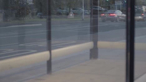 Punto-De-Vista-De-La-Ciudad-Urbana,-Tráfico-Al-Atardecer-A-Través-De-Las-Ventanas-De-Las-Paradas-De-Autobús