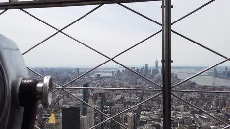 Vista-De-La-Ciudad-De-Nueva-York-Desde-El-Edificio-Empire-State---Gimbal-Moviéndose-A-Través-De-La-Cerca-Junto-A-Binoculares-Que-Funcionan-Con-Monedas-En-La-Plataforma-De-Observación-En-Un-Día-Soleado-De-Verano-4k