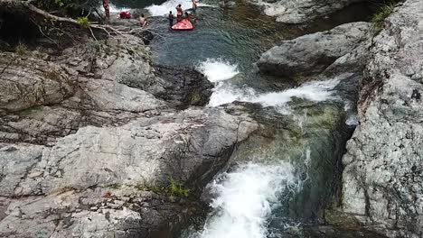 People-Under-Cascade-of-Waterfall,-Slow-Motion-Aerial-View