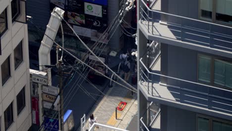 People-walking-along-a-commercial-street-with-stores-and-signs,-Stable-high-view-shot