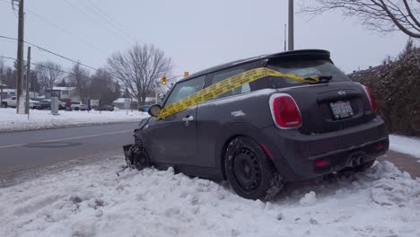 Small-vehicle-wrapped-in-police-tape-post-accident-and-in-snow-on-side-of-road-in-winter