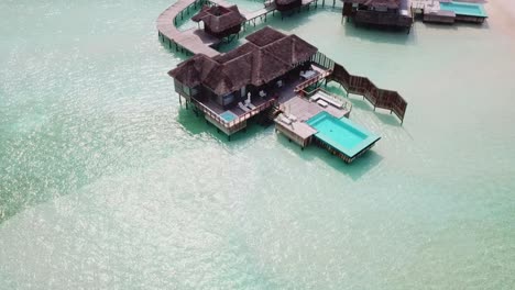 Aerial,-reverse,-drone-shot,-away-from-a-bungalow-with-a-pool-and-a-white-sand-beach,-surrounded-by-swallow,-turquoise-sea,-on-a-sunny-day,-on-the-Conrad-Rangali-island,-in-Maldives