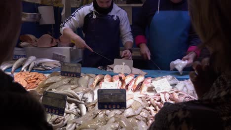 Cámara-Lenta,-Los-Vendedores-De-Pescado-Fresco-Limpian-El-Pescado-En-El-Puesto-Del-Mercado-Mientras-Los-Clientes-Hablan