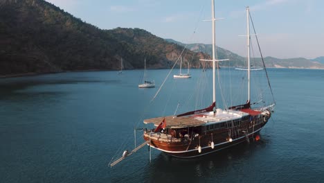 Drone-flying-close-to-boat-moored-in-bay-in-Mediterranean-sea,-vibrant-turquoise-water