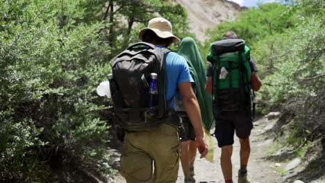 Tiro-De-Seguimiento-Cercano-De-Excursionistas-Bien-Equipados-Con-Mochilas-Mientras-Caminan-En-La-Naturaleza-En-Un-Día-Soleado