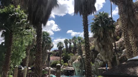 handheld-wide-shot-of-a-pool-lagoon-area-in-Avalon-Springs-Resort-Hotel-on-a-sunny-day-with-blue-sky-and-puffy-clouds