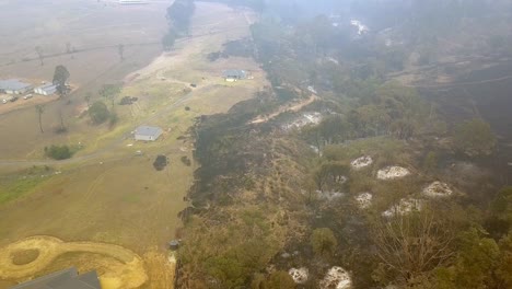 Homes-near-burnt-fire-line-from-nearby-eucalyptus-forest-blaze,-Aerial-drone-lowering-approach-shot