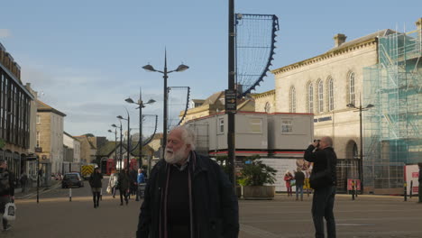 Hall-for-Cornwall,-Lemon-Quay,-Truro,-United-Kingdom---An-Old-Man-With-Cane,-Slowly-Walking-On-The-Streets-With-Busy-Tourists-On-The-Background---Wide-Shot