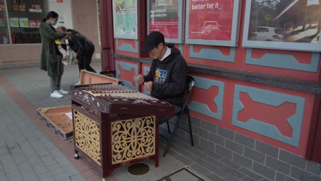 Ein-Kleiner-Junge-Und-Eine-Mutter-Mit-Einem-Baby-Geben-Münzen-An-Einen-Alten-Asiatischen-Straßenmusiker,-Der-In-Cabramatta-Ein-Yangqin-Oder-Chinesisches-Hackbrett-Spielt