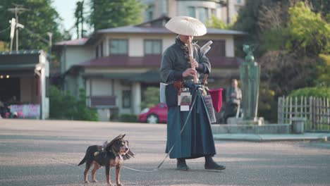 Famoso-Flautista-Samurái-Japonés-Tocando-Shakuhachi-Con-Su-Perro-Samurái-Frente-A-Los-Turistas-En-El-Parque-Maruyama-Al-Lado-Del-Santuario-Yasaka-En-Kyoto,-Japón