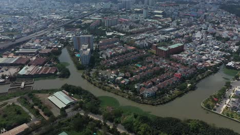 Fly-in-view-over-canal,-industrial-buildings-and-residential-buildings-with-roads,-parklands-and-canals-on-a-sunny-day