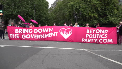 Más-Allá-De-La-Política,-Los-Manifestantes-Ambientales-Bloquean-Un-Cruce-De-Carreteras-En-Trafalgar-Square-Con-Una-Gran-Pancarta-De-Color-Rosa-Brillante-Que-Dice-&quot;derribar-Al-Gobierno&quot;